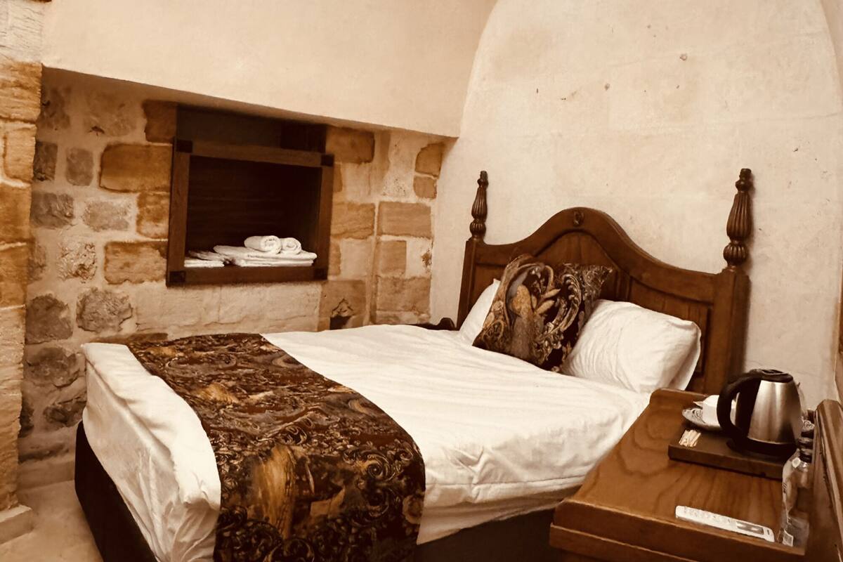 A bedroom with a stone wall, a wooden bed, a nightstand, and a small shelf with towels.