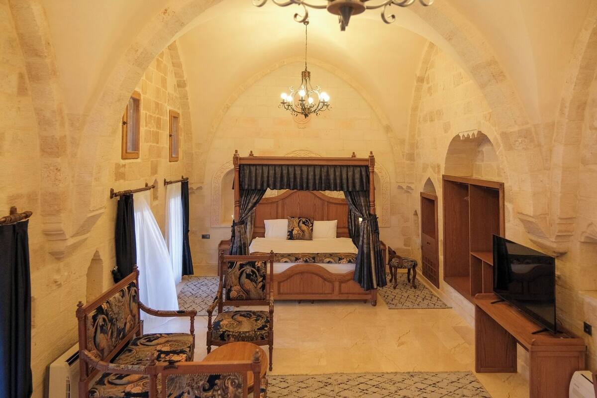 A bedroom with a four-poster bed, a chandelier, and a television.