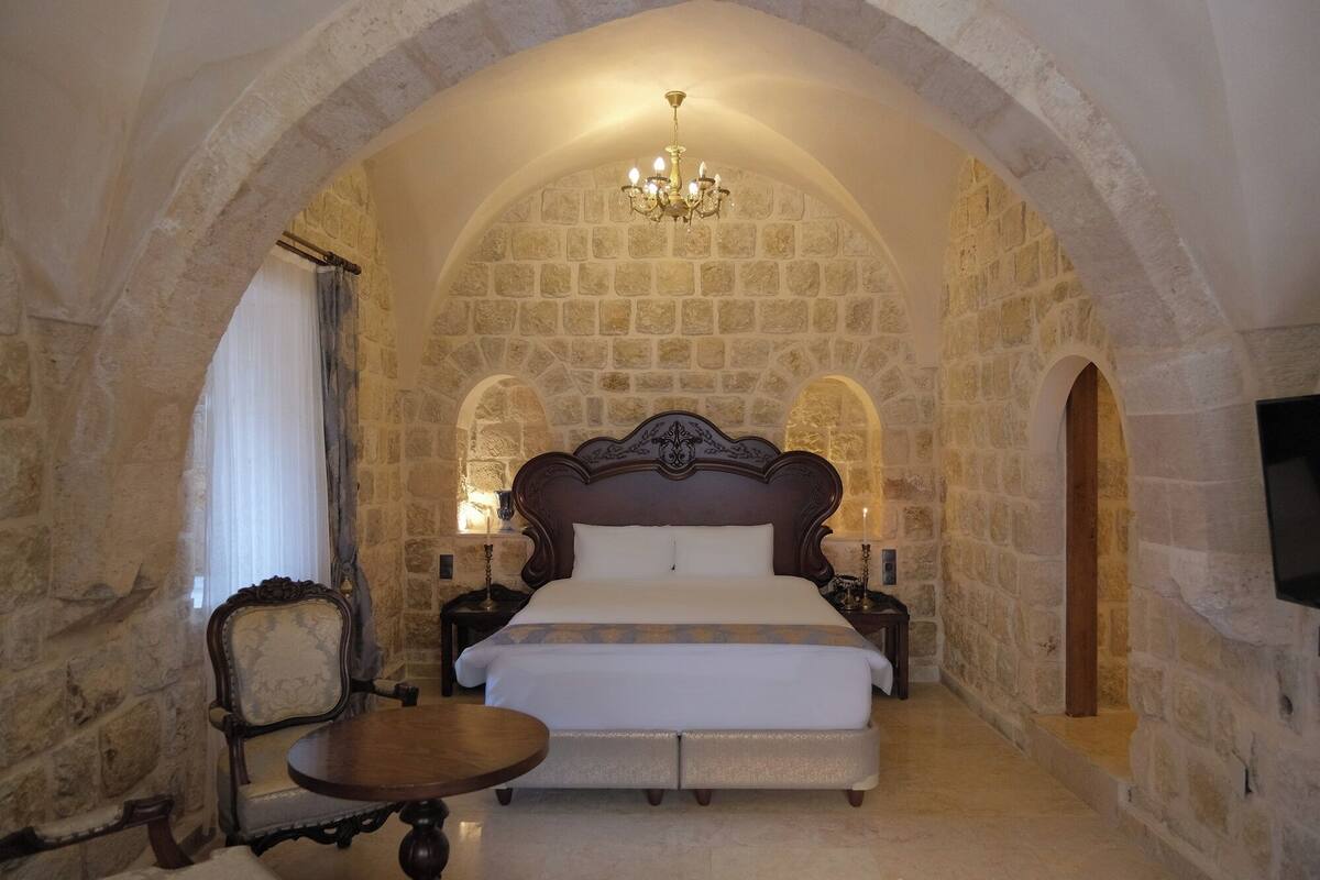 A bedroom with a stone wall, a bed, a chandelier, and a small table.