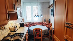 A kitchen with wooden cabinets, a gas stove, a round dining table with chairs, and a window with curtains. - Charming Vintage Vienna Getaway  67m² with A/C (Wien)