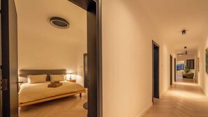 Ein modernes Hotelzimmer mit einem großen Bett, Nachttischen und einem Flur, der zu weiteren Zimmern führt.