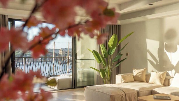 Ein modernes Wohnzimmer mit einer großen Couch, einem Couchtisch und Blick auf eine Stadtlandschaft durch einen Balkon.