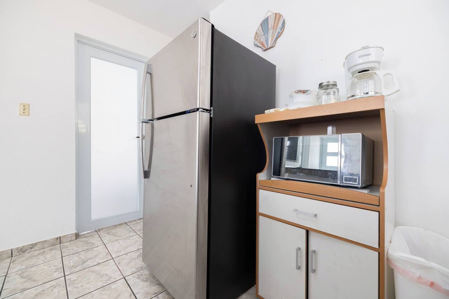 Een compacte keuken met een roestvrijstalen koelkast, een magnetron en een koffiezetapparaat op een houten plank.