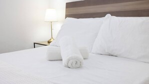 Ein ordentlich bezogenes Bett mit weißen Bettwäsche und Handtüchern, einer Nachttischlampe und einem hölzernen Kopfteil.
