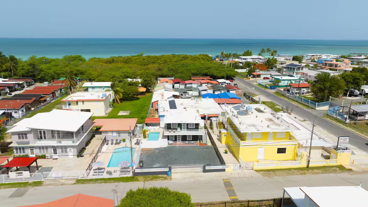 A coastal residential area with houses, a swimming pool, and a road leading to the beach.