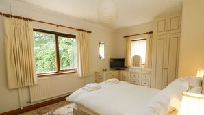 Ein Schlafzimmer mit einem großen Bett, einem Fernseher, einem Schminktisch und einem Fenster mit Vorhängen.