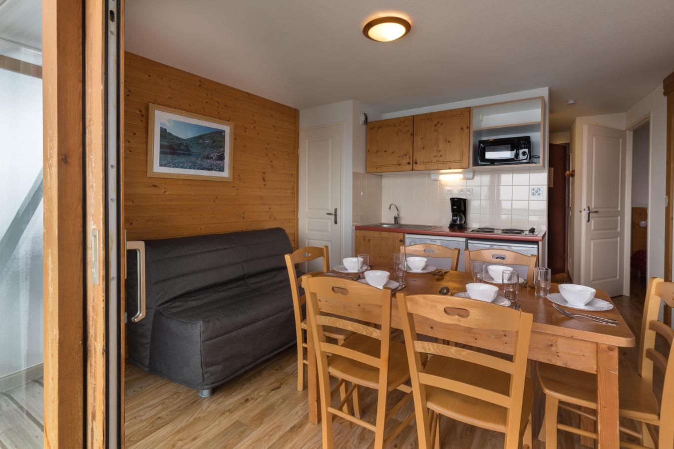 A compact kitchen with wooden cabinets, a microwave, and a dining area with a table set for four.