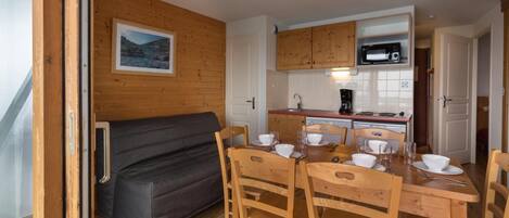 A compact kitchen with wooden cabinets, a microwave, and a dining area with a table set for four.
