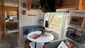 Ein kompaktes Wohnmobil-Interieur mit Küchenzeile, einer Sitzecke mit Tisch und einem an der Wand befestigten Fernseher.