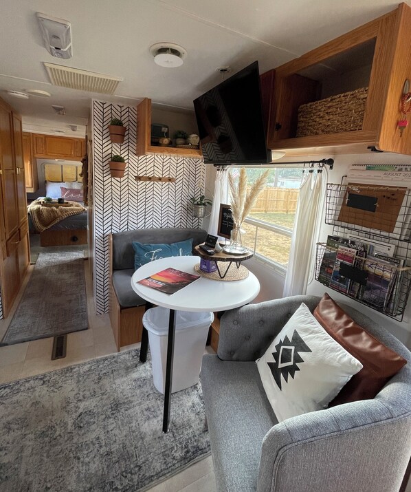 A compact RV interior with a kitchenette, a seating area with a table, and a mounted TV.