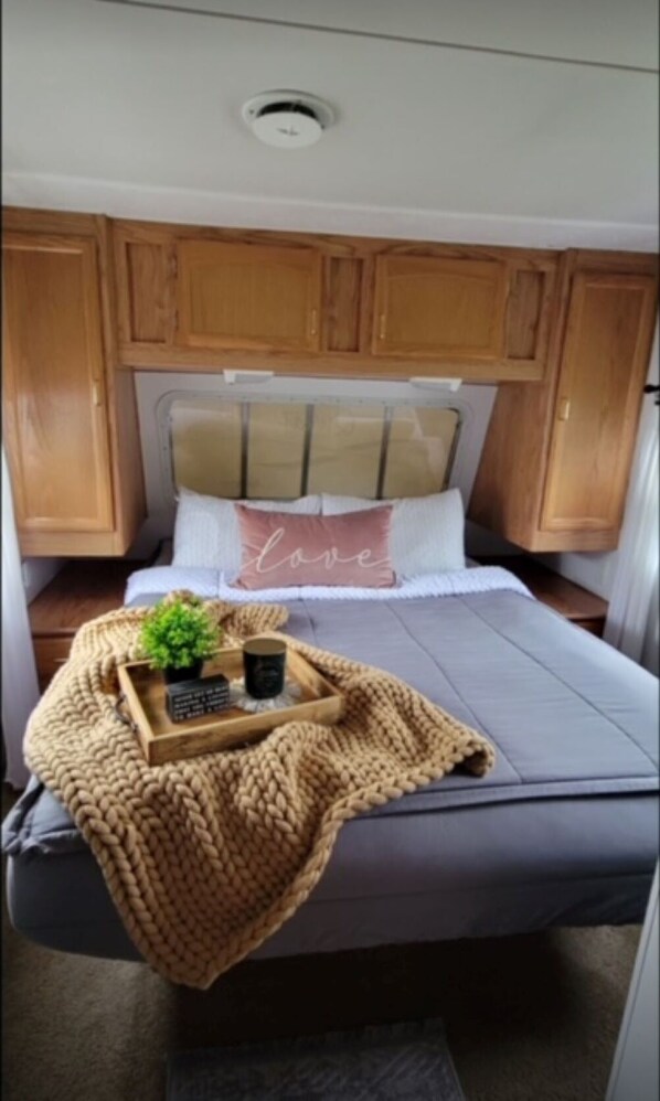 A cozy RV bedroom with a bed, wooden cabinets, a headboard, and a bedside table with a tray.