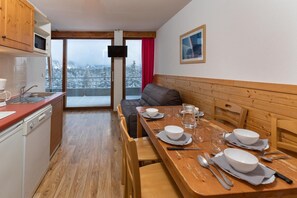 A cozy dining area with a wooden table set for four, a sofa, and a kitchen with a microwave and sink.