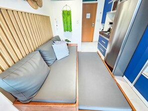 Een ruimtelijke leefruimte met een bank, een kleine keuken en een deur naar een andere kamer.