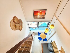 A staircase leading to a room with a view of a swimming pool, a dining area with blue chairs, and a framed picture on the wall. - Condomínio Bela Vista Porto de Galinhas (Ipojuca)