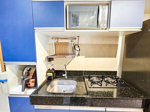 A compact kitchenette with a microwave, sink, and gas stove. - Condomínio Bela Vista Porto de Galinhas (Ipojuca)