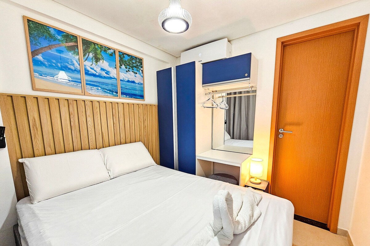 A hotel room with a bed, a wooden headboard, a blue wardrobe, a mirror, a hanging light, and a door.