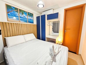 A hotel room with a bed, a wooden headboard, a blue wardrobe, a mirror, a hanging light, and a door. - Condomínio Bela Vista Porto de Galinhas (Ipojuca)