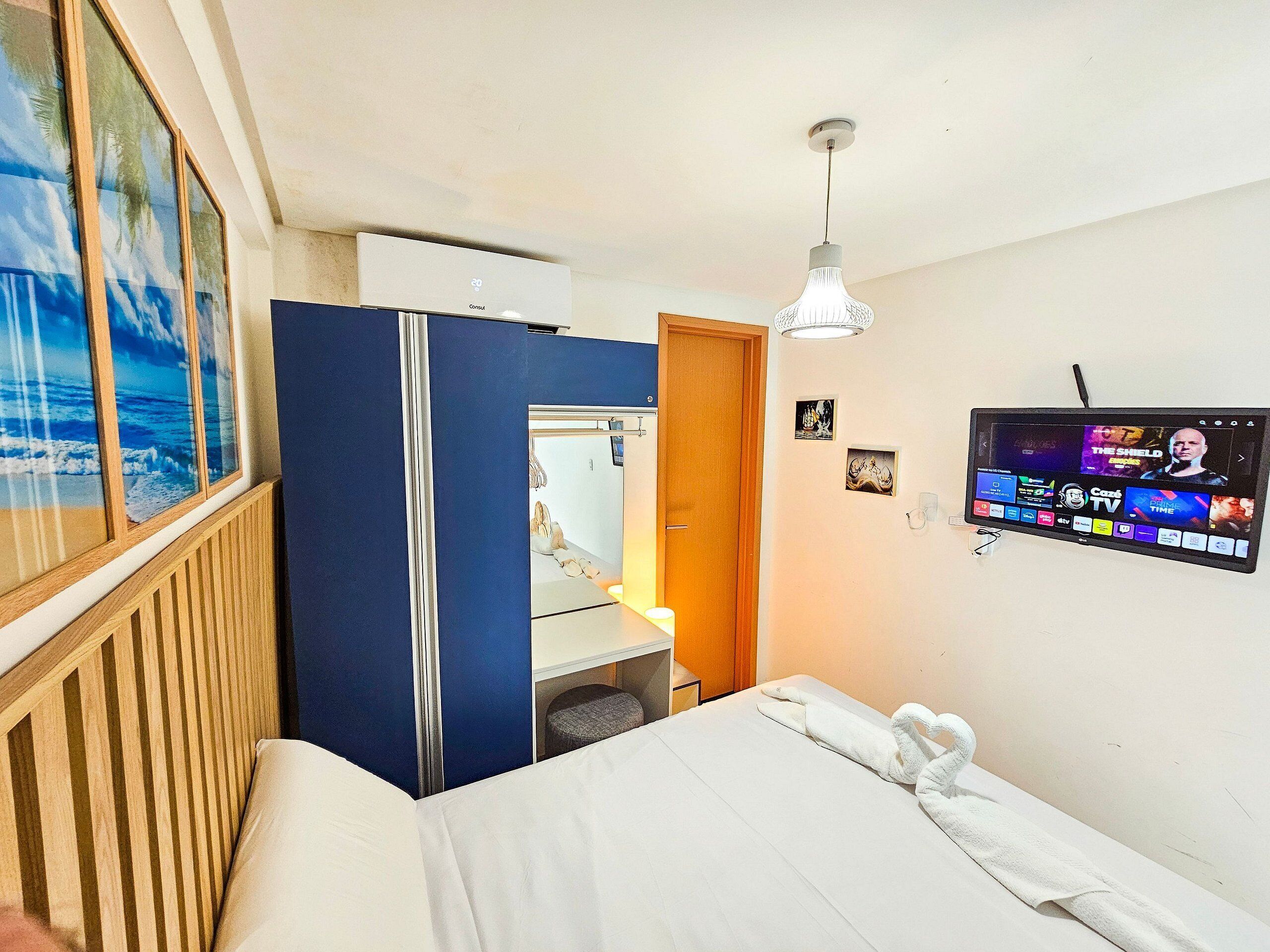 A hotel room with a bed, a TV mounted on the wall, a wardrobe, and a window with a view of the sea.