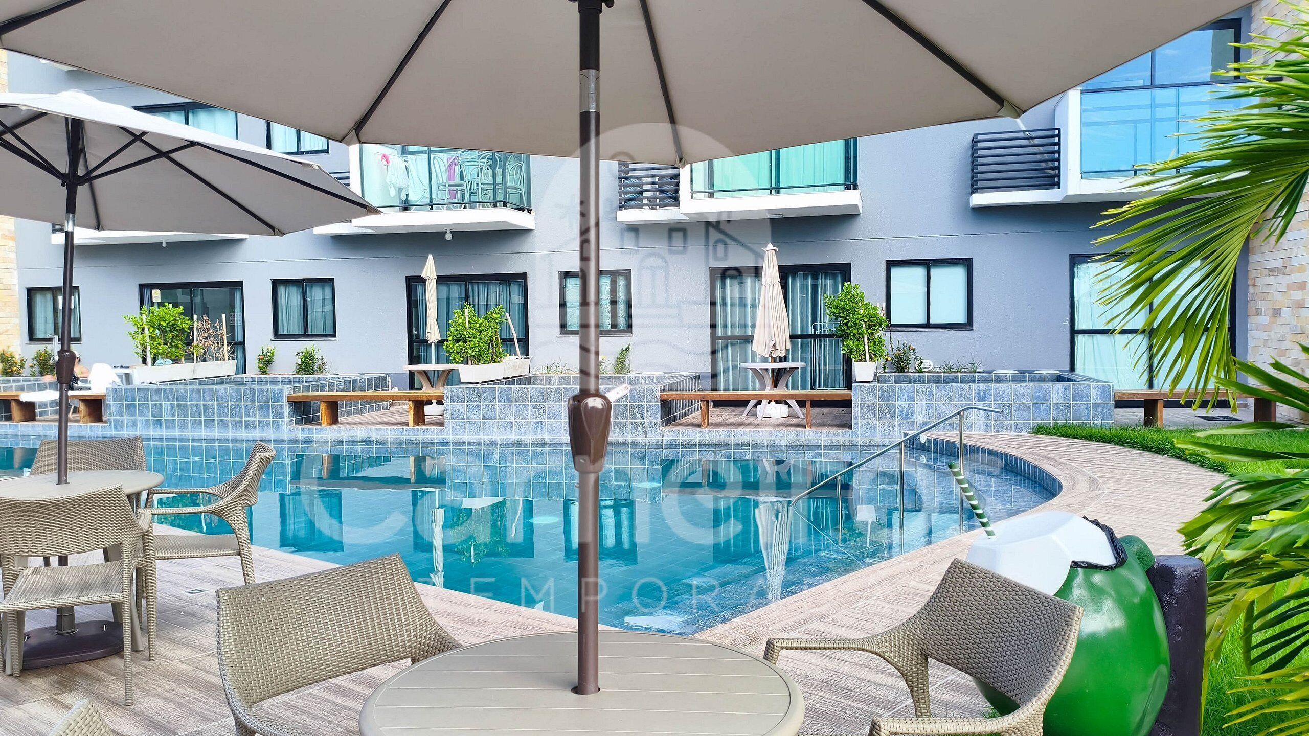 Un área de piscina moderna con sillones de descanso, una mesa y sombrillas.