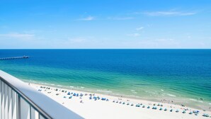A beach with clear blue water, a pier, and numerous umbrellas on the sand. - Premium Condo Beachfront Lazy River-Water slide-Splash Pad-Walk to Restaurants (Gulf Shores)
