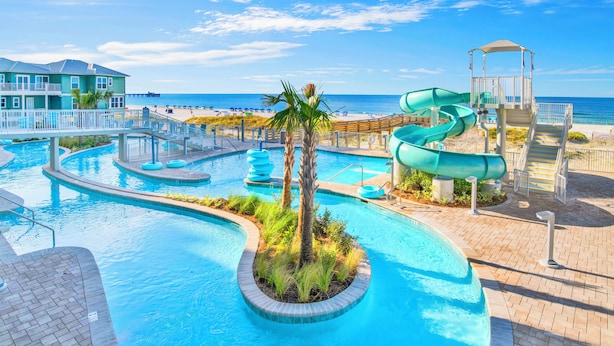 A swimming pool with a slide, palm trees, and a view of the beach. - Premium Condo Beachfront Lazy River-Water slide-Splash Pad-Walk to Restaurants (Gulf Shores)