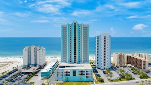 A beachfront hotel with a central tower, multiple smaller buildings, and a parking lot. - Premium Condo Beachfront Lazy River-Water slide-Splash Pad-Walk to Restaurants (Gulf Shores)