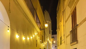 Eine enge Kopfsteinpflasterstraße bei Nacht mit Lichterketten, weißen Gebäuden und Balkonen.