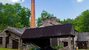 Un bâtiment historique doté d’une haute cheminée en briques, de murs en pierre et d’un toit en métal.