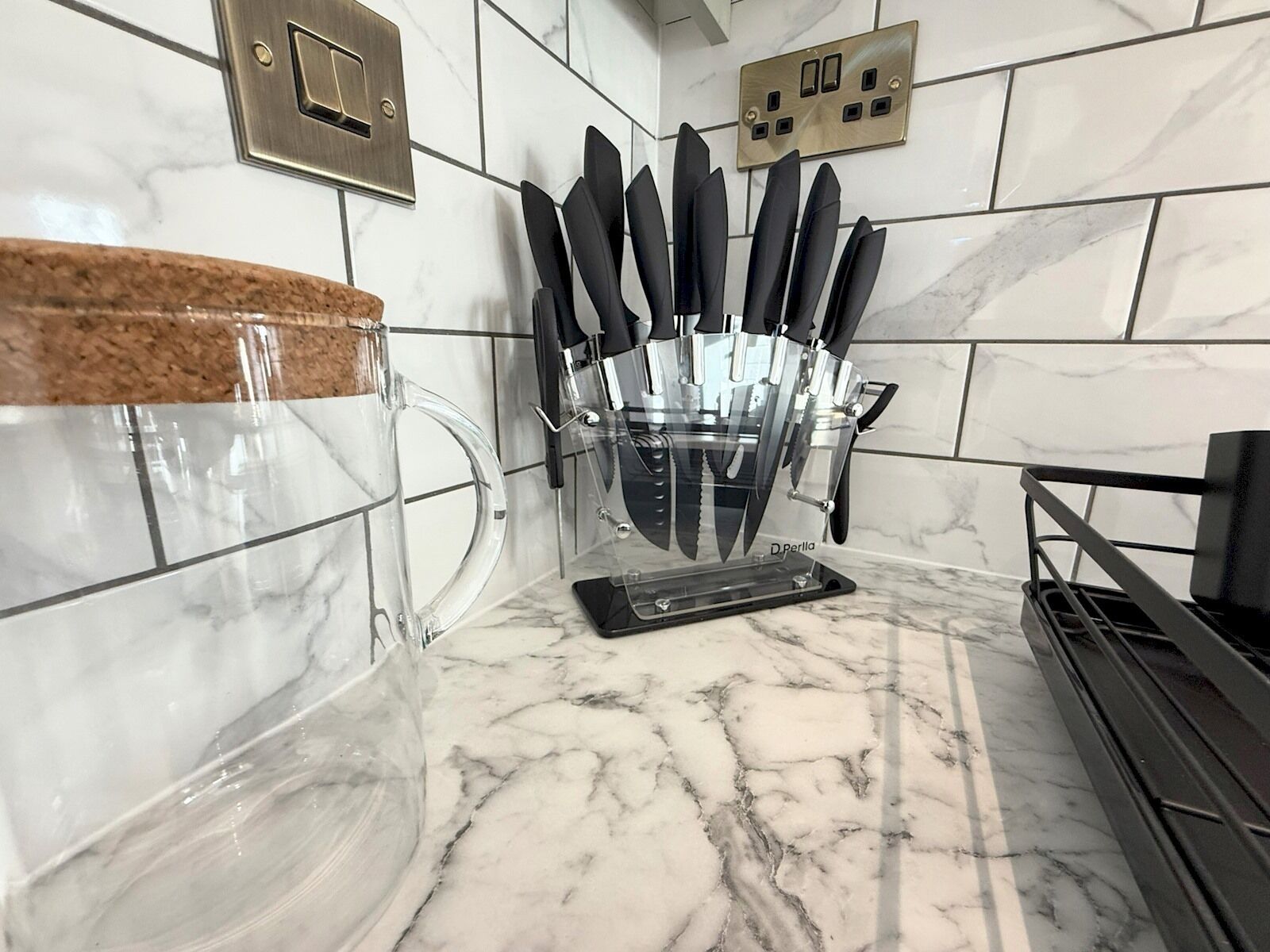 Una cocina con encimera de mármol, una jarra de vidrio con tapón de corcho y un bloque de cuchillos negros.