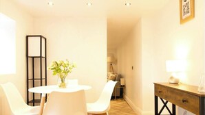 A dining area with a round table and four chairs, a vase with flowers, a lamp, and a wooden bench with a chessboard. - Bubbles & Bliss - Hot Tub/Garden | Pass the Keys (Rye)