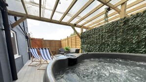 A hot tub area with a wooden deck, two striped lounge chairs, and a wall covered with foliage. - Bubbles & Bliss - Hot Tub/Garden | Pass the Keys (Rye)