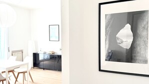 Ein modernes Zimmer mit einem weißen Esstisch, einem schwarzen Schrank und einem Bilderrahmen mit einer Küstenansicht.