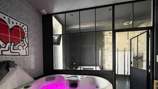 A modern bathroom with a large mirror, a hot tub with purple lighting, and a view of a stone wall and outdoor area. - A charming gite (Sainte-Luce-sur-Loire)