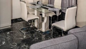 Un espace repas avec une table en verre, des chaises blanches, un lustre et un motif décoratif sur le mur.
