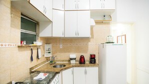 Una cocina con armarios blancos, encimera de granito, pileta de acero inoxidable, estufa, cafetera y refrigerador.
