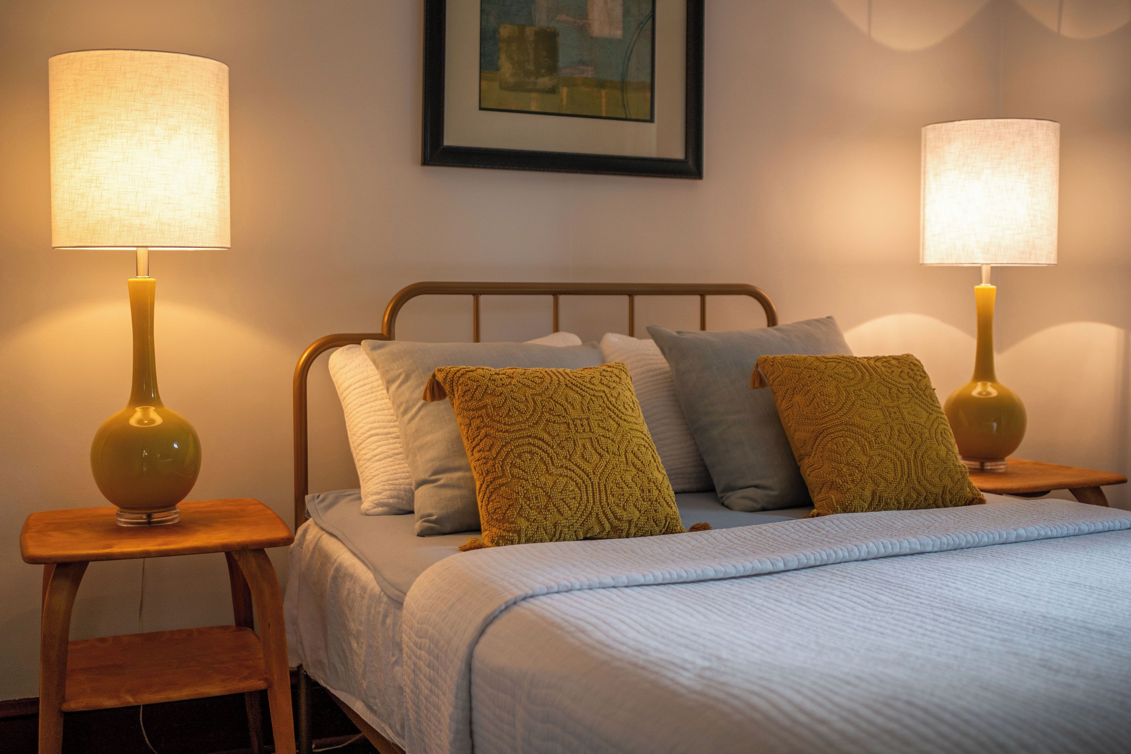 Un lit bien fait, avec une couverture bleue, deux lampes de chevet et des coussins à motifs.