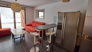 Eine moderne Küche mit einem Edelstahlkühlschrank, einer Bar mit Barhocker und einem roten Sofa.