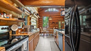 A log cabin kitchen with wooden cabinets, a stove, a refrigerator, and a dining table with chairs.