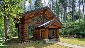 A log cabin with a large porch, stone steps, and a fire pit.