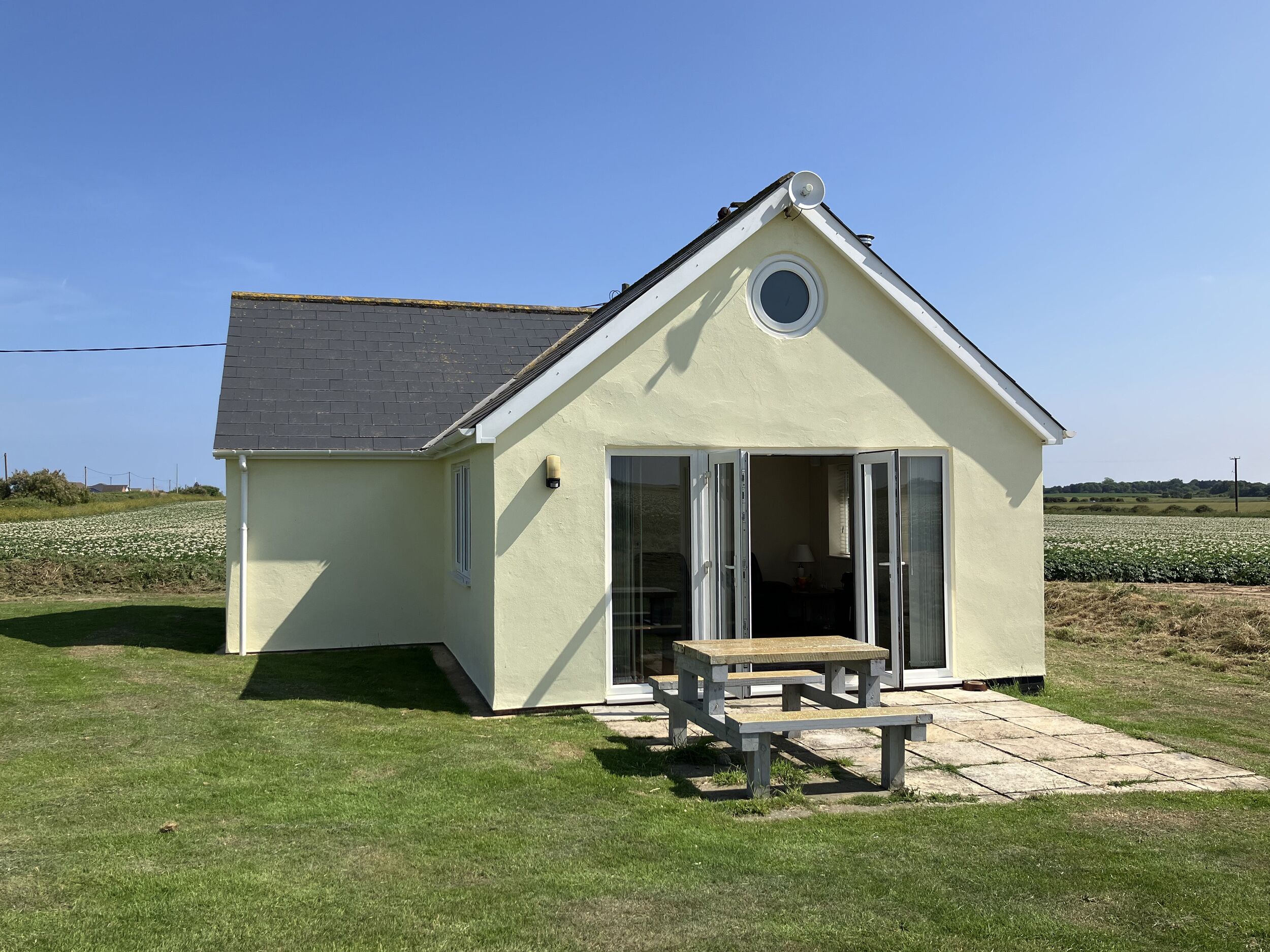 A small, single-story house with a sloped roof and a circular window. It has a sliding glass door leading to an interior with a visible table and chair.
