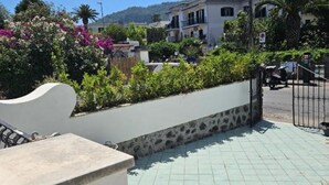A paved outdoor area with a stone wall, a metal railing, and a view of residential buildings in the background.