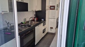 A narrow kitchen with white cabinets, a black countertop, and a tiled backsplash.