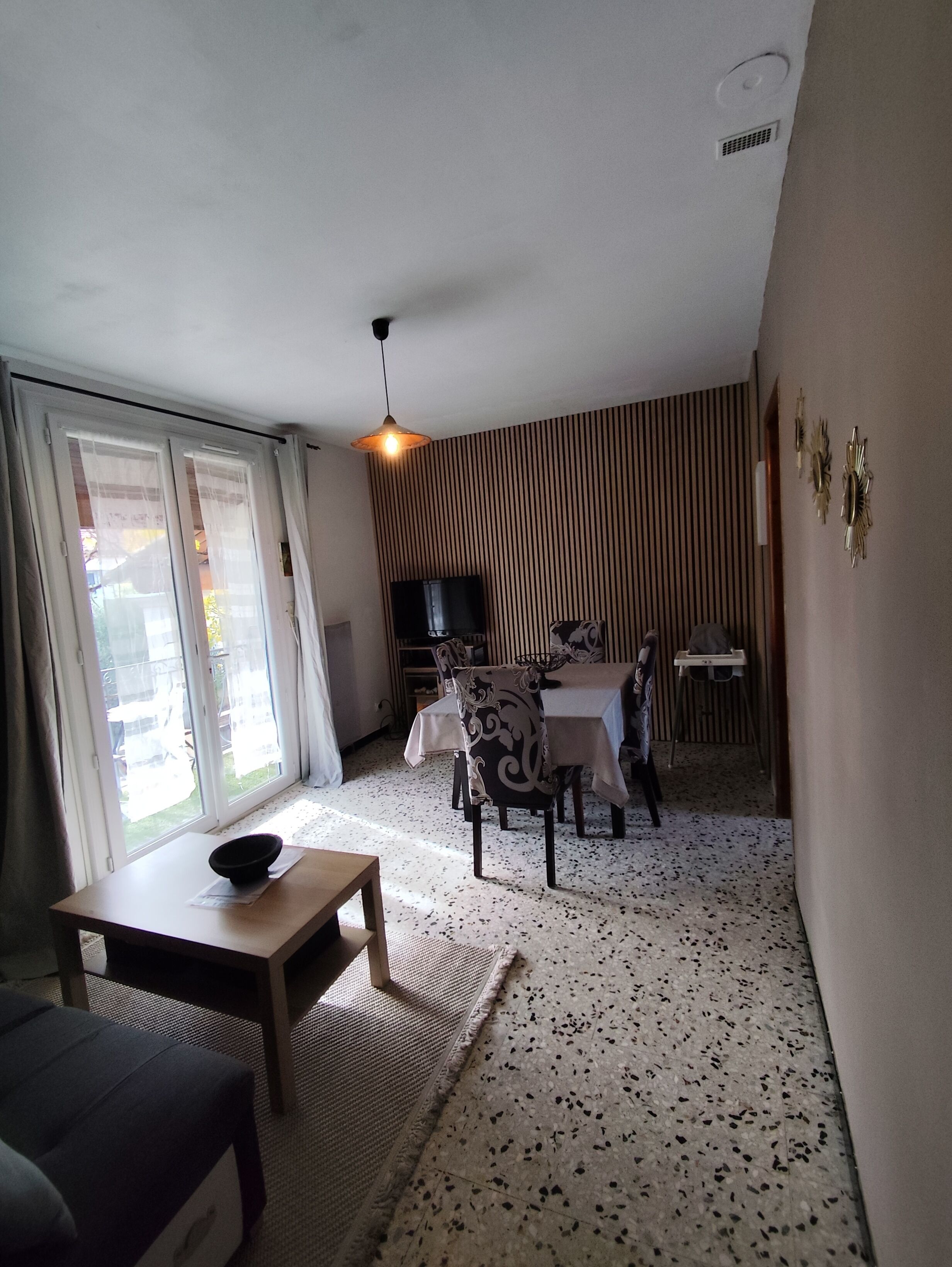 Un salon comprenant un coin repas, un téléviseur et une fenêtre avec des rideaux.