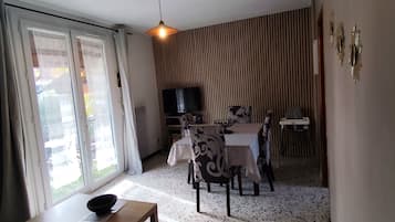 Un salon comprenant un coin repas, un téléviseur et une fenêtre avec des rideaux.