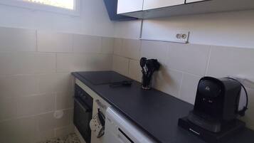 A compact kitchen with white cabinets, a black countertop, a coffee maker, and a dishwasher.
