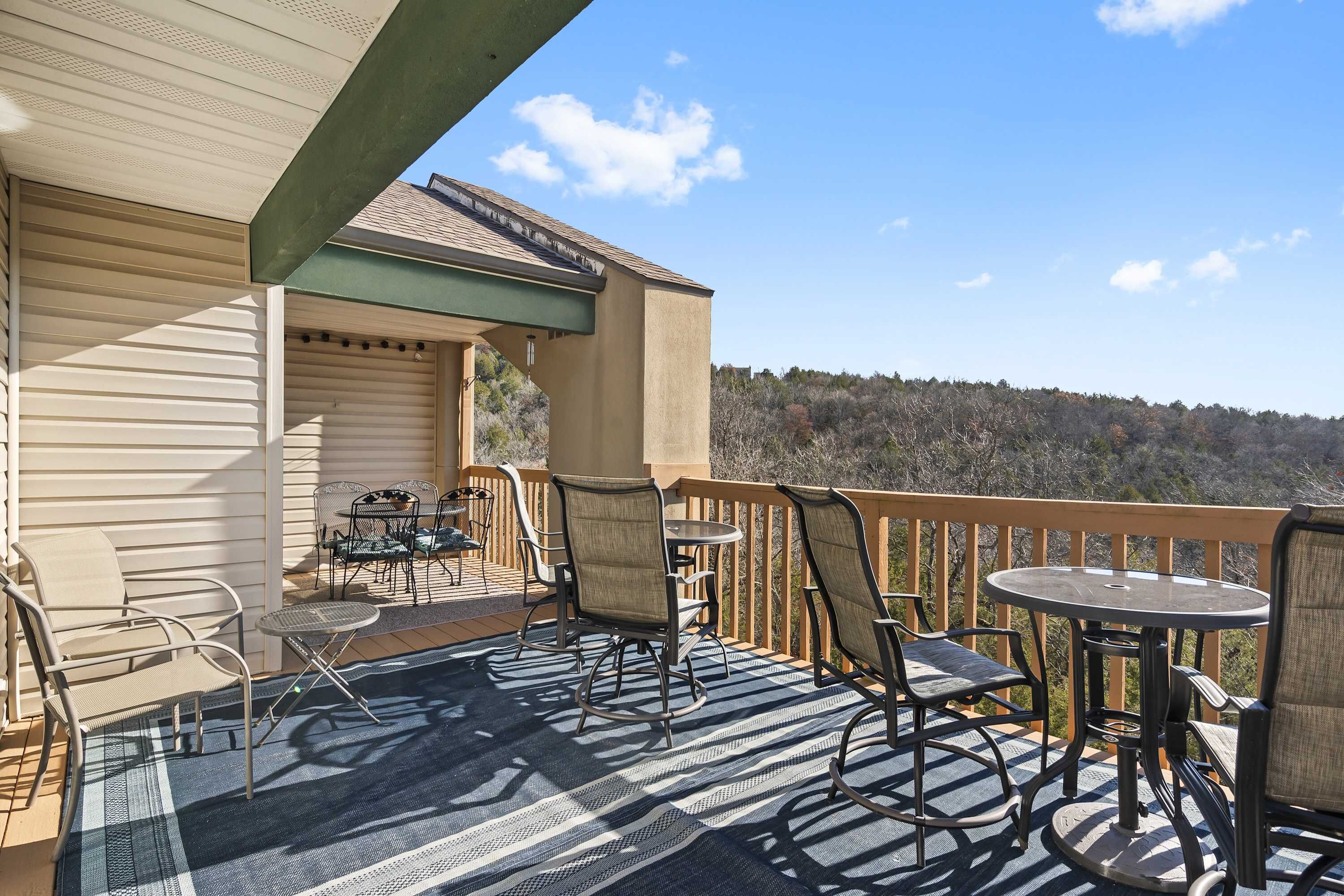 A covered outdoor deck with seating and a table, overlooking a forested area.