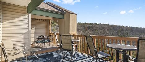 A covered outdoor deck with seating and a table, overlooking a forested area.