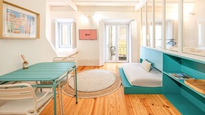 Une pièce de taille modeste comprenant un lit, une petite table, une chaise, une fenêtre et une porte donnant sur un balcon extérieur.