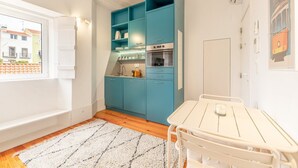 Une cuisine compacte avec des meubles de couleur turquoise, un plan de travail blanc et un petit coin repas comprenant une table et des chaises.