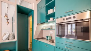 A compact kitchen with teal cabinetry, a stainless steel oven, and a built-in microwave. - GuestReady - Esperança do Cardal 2D (Lisbon)